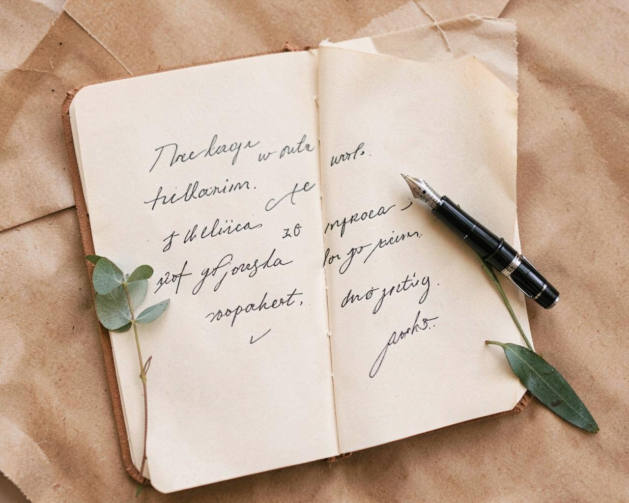 Overhead of a handwritten vow book with a fountain pen and eucalyptus sprig
